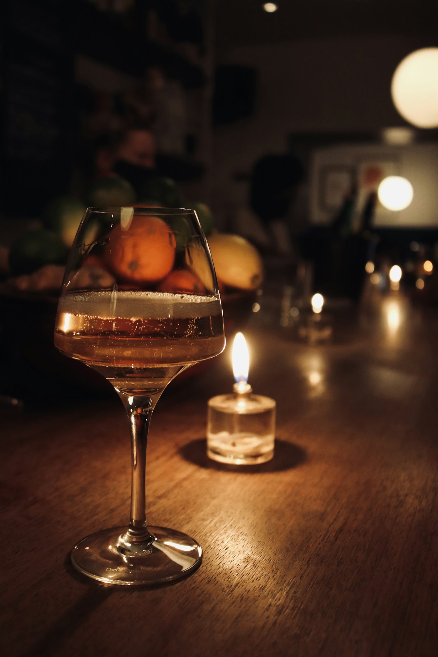 Stemningsbilde. Vinglass og levende lys på et trebord i dempet lys.